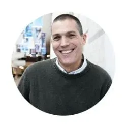 Smiling man with short hair wearing a dark sweater in an indoor setting.