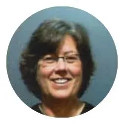 A smiling middle-aged woman with short dark hair and glasses, against a blue background.